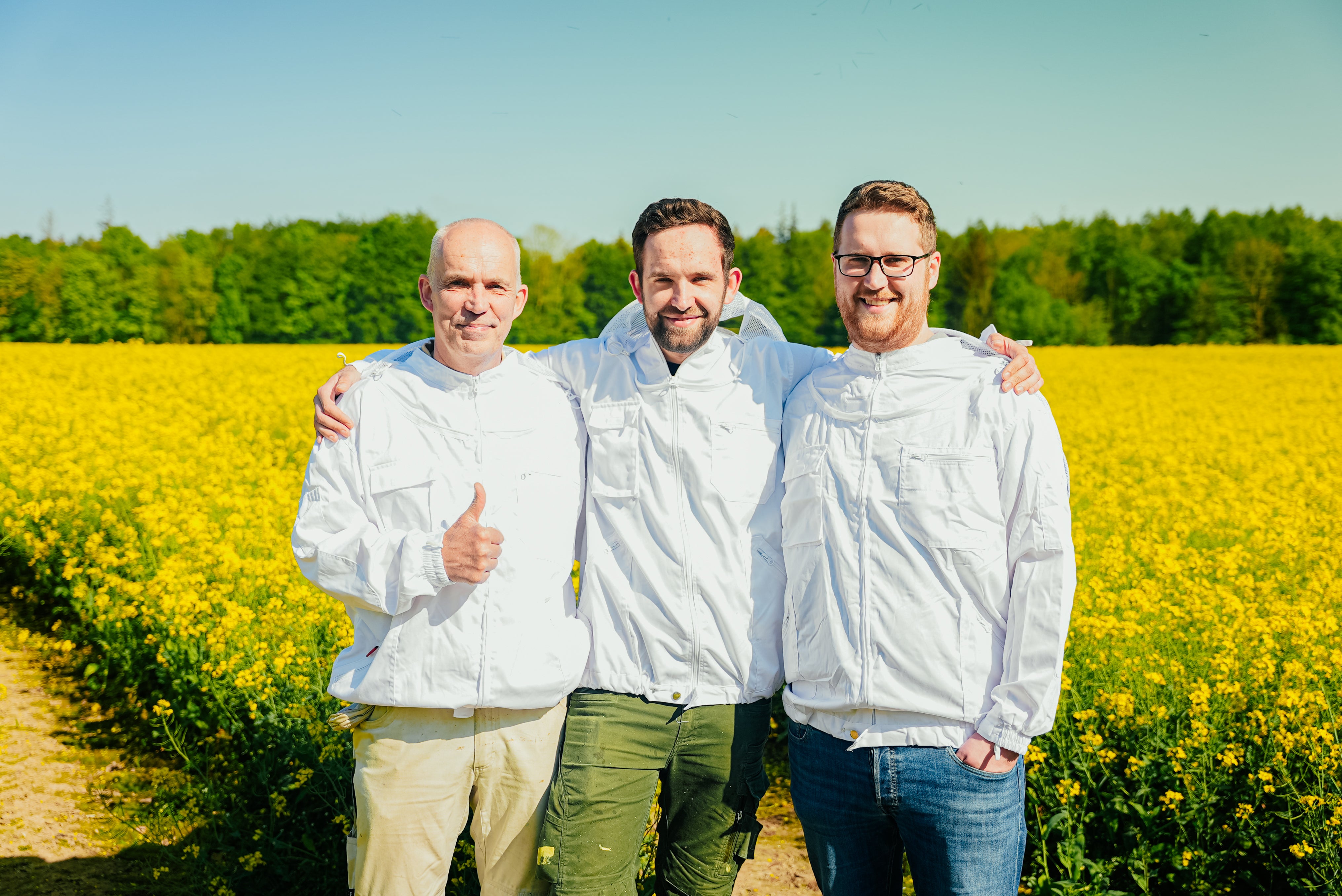 Auf dem Foto sind die Gründer der Imkerei Arndt zu sehen, welche in einem blühenden Rapsfeld stehen. (Links Peter Arndt, Mitte Peer Arndt und rechts Hauke Arndt)