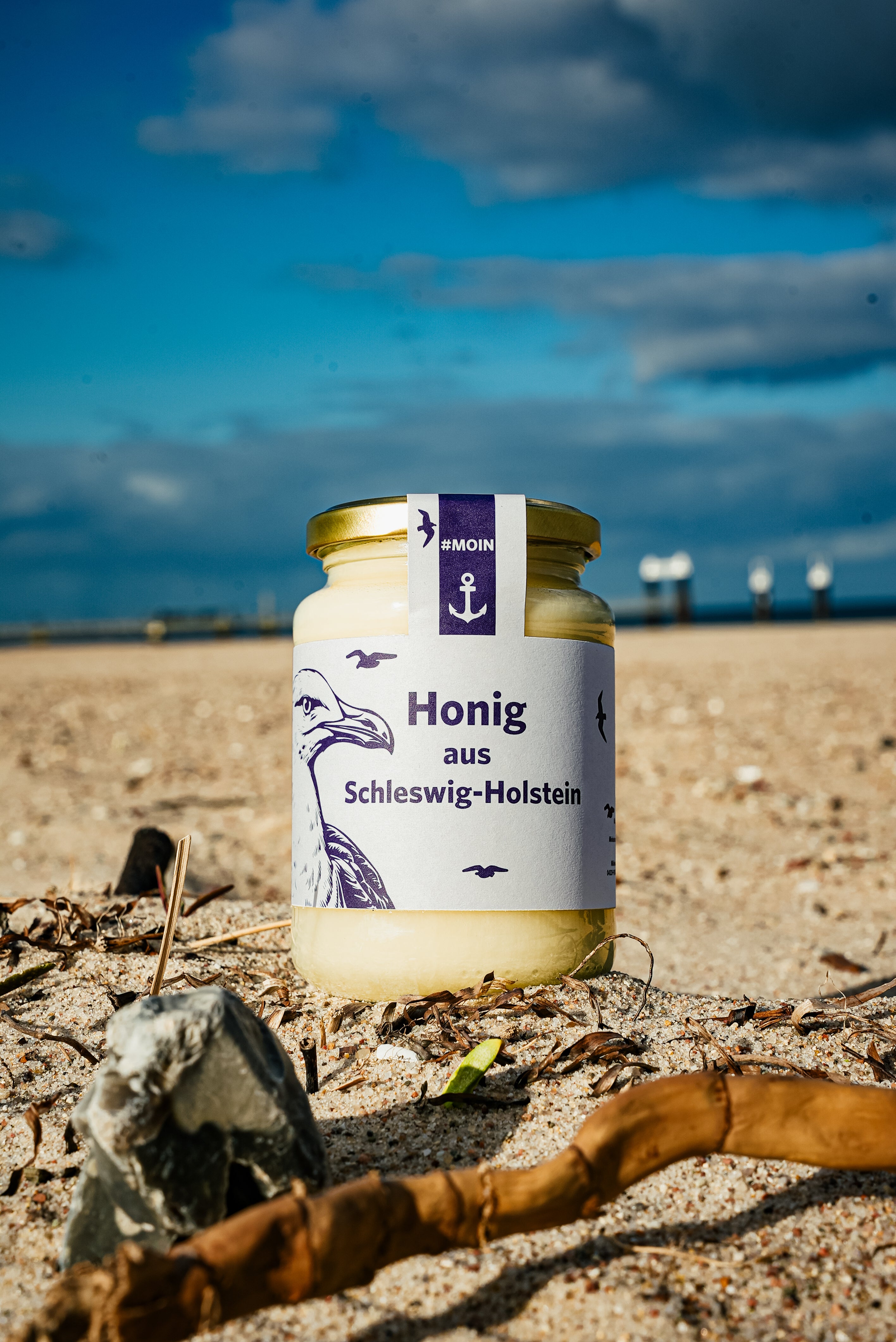 Auf dem Bild ist ein Glas Rapshonig in einem Norddeutschen Motiv mit einer abgebildeten Möwe zu sehen, welches sich am Strand befindet.